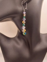 Load image into Gallery viewer, A pair of long dangling earring displayed on a black mannequin bust. The earring has a silver kidney ear wire  and a vertical drop of faceted beads in green, golden and clear tones, set against a plain light background. 
